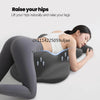 A woman is lying down, using a gray ergonomic memory foam pillow to raise her hips and legs.