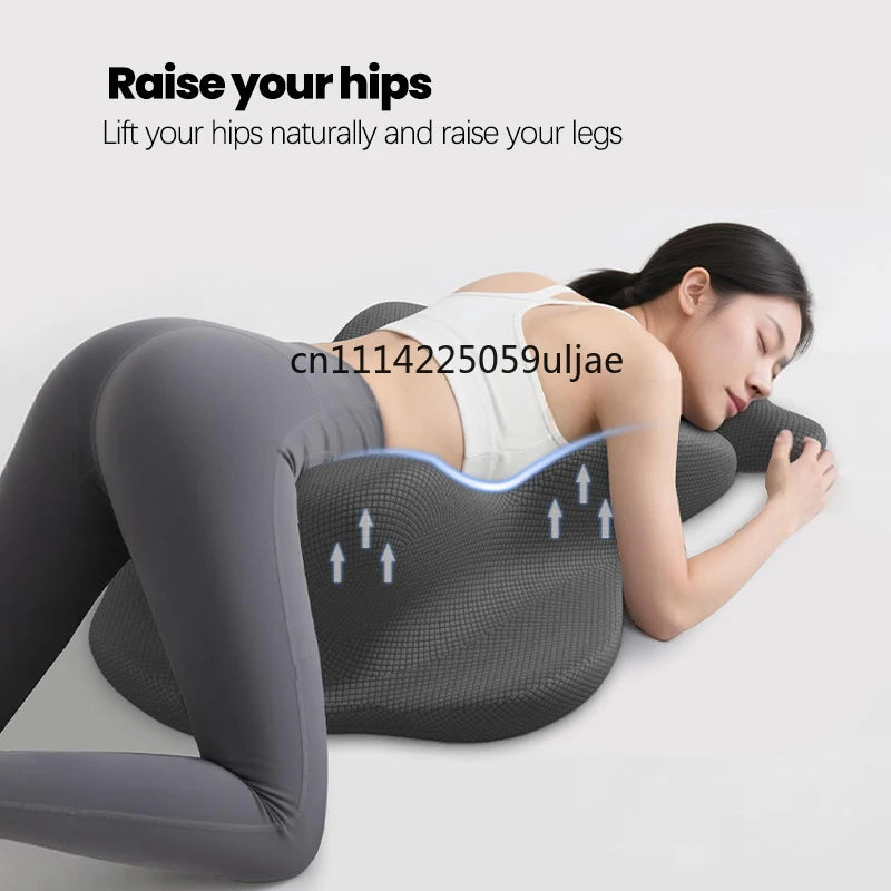 A woman is lying down, using a gray ergonomic memory foam pillow to raise her hips and legs.