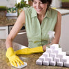 A woman is using yellow cleaning gloves to handle white melamine sponge cleaning erasers on a countertop.
