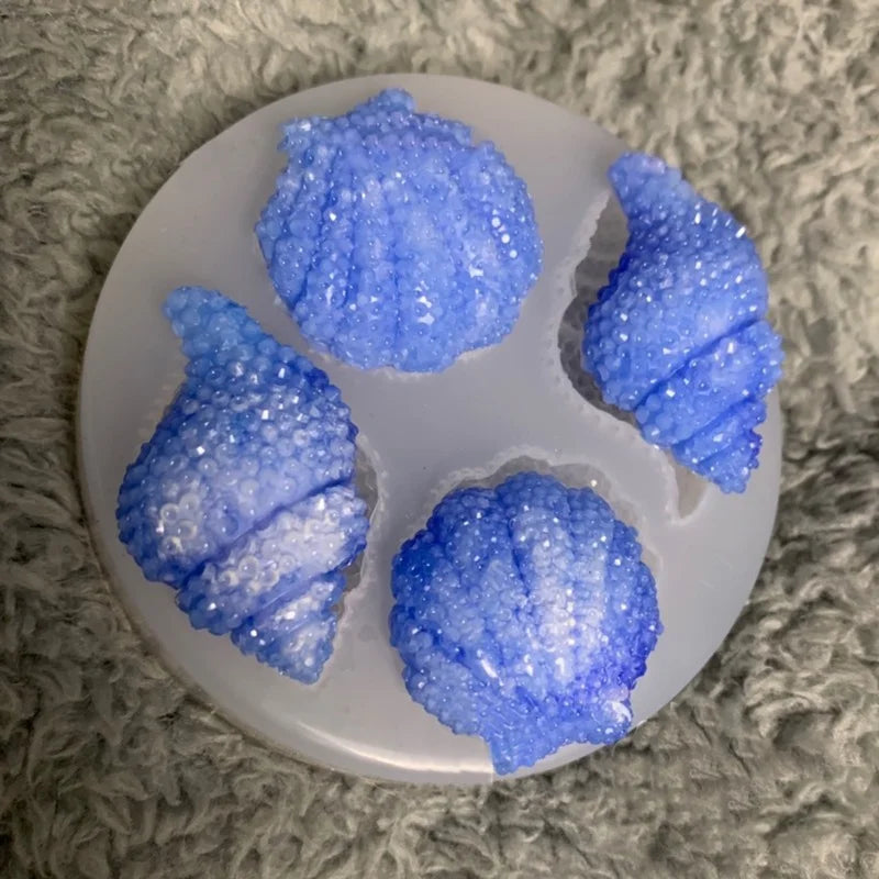 A set of blue iridescent shell and starfish fondant molds for cake decorating displayed on a white plate.