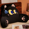 A black cat plush backrest cushion with yellow and blue eyes rests on a wooden surface.