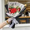 A bouquet of red and white artificial flowers with a sign reading Love is Life presented in a black holder.