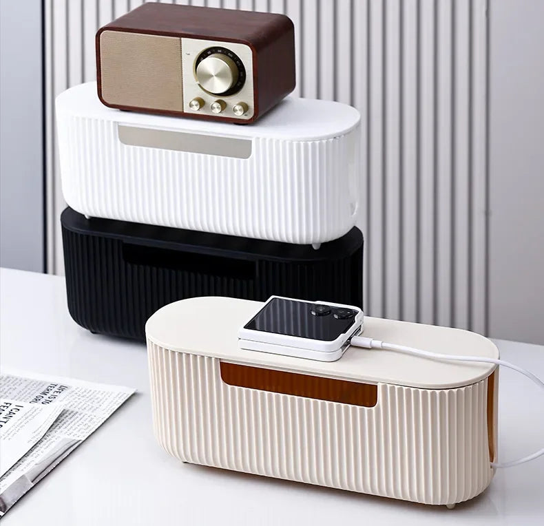 A set of modern cable management boxes in brown, white, and black are displayed on a white desk.