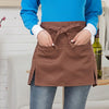 A person wearing a brown half apron with tie closure and pockets over a blue shirt and jeans.