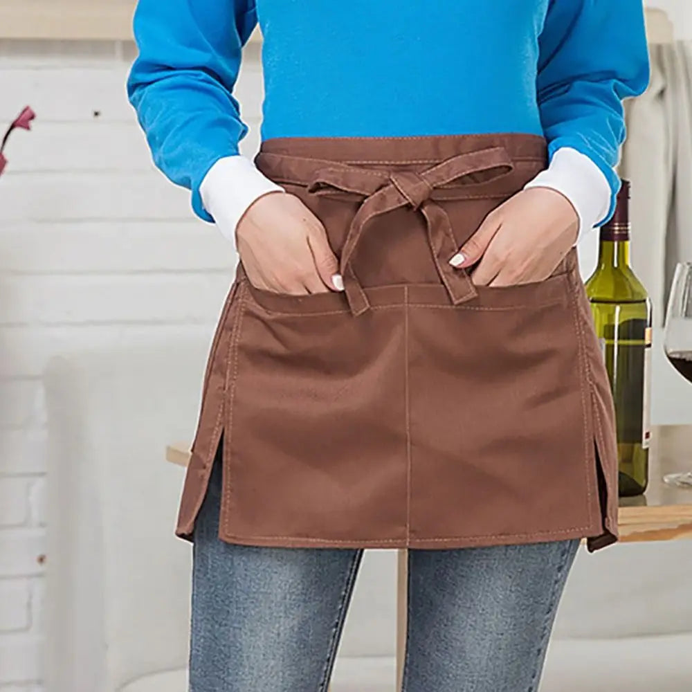 A person wearing a brown half apron with tie closure and pockets over a blue shirt and jeans.