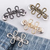 A collection of adjustable clover waist tightener buckles in silver and gold tones displayed on a denim fabric.