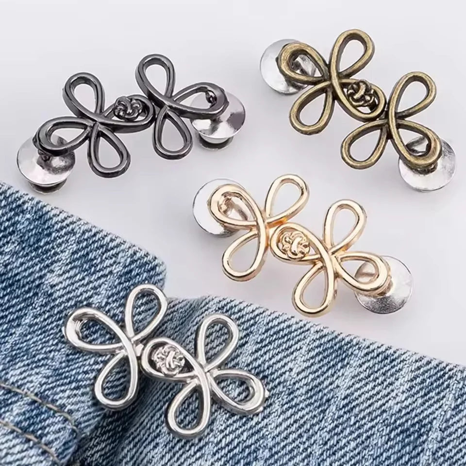 A collection of adjustable clover waist tightener buckles in silver and gold tones displayed on a denim fabric.