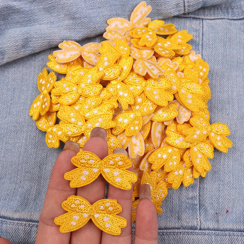 A hand holds a cluster of yellow and white embroidered cartoon bow iron-on patches for DIY clothing decoration.