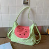 A light green nylon messenger bag shaped like a watermelon slice is displayed on a wooden surface.