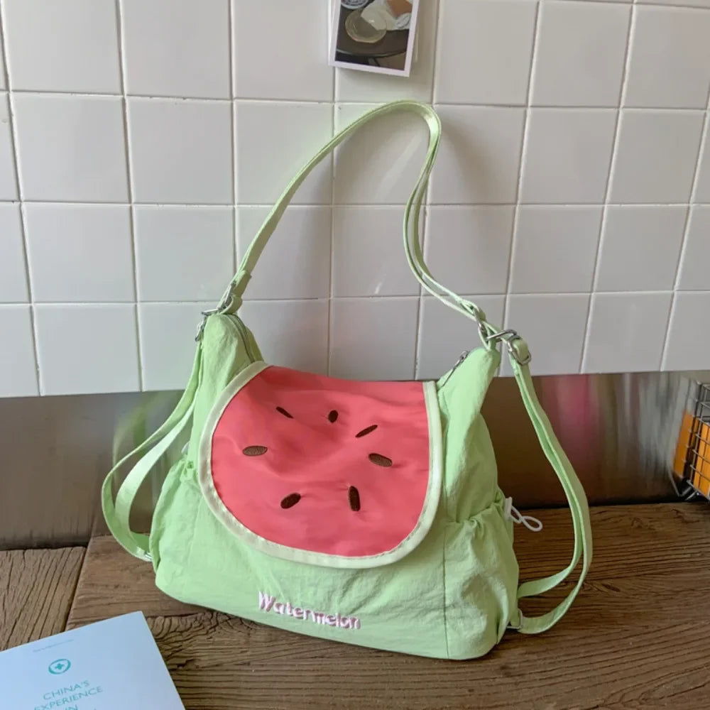 A light green nylon messenger bag shaped like a watermelon slice is displayed on a wooden surface.