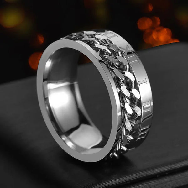 Primer plano de un anillo spinner de acero inoxidable con diseño de malla de cadena sobre una superficie oscura.