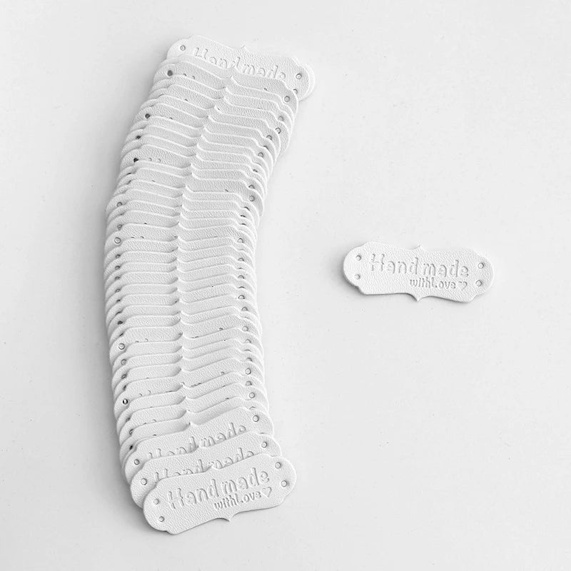 A stack of white PU leather sewing labels with 'Hand made with love' text for handmade crafts.