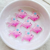 Pink glitter resin charms shaped like fish with small flower accents arranged in a white bowl