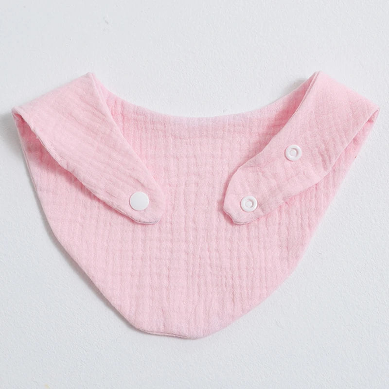 A pink organic cotton muslin baby bib with a gathered collar and buttons.
