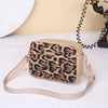 A beige leopard print crossbody bag with a tan strap resting on a white surface.