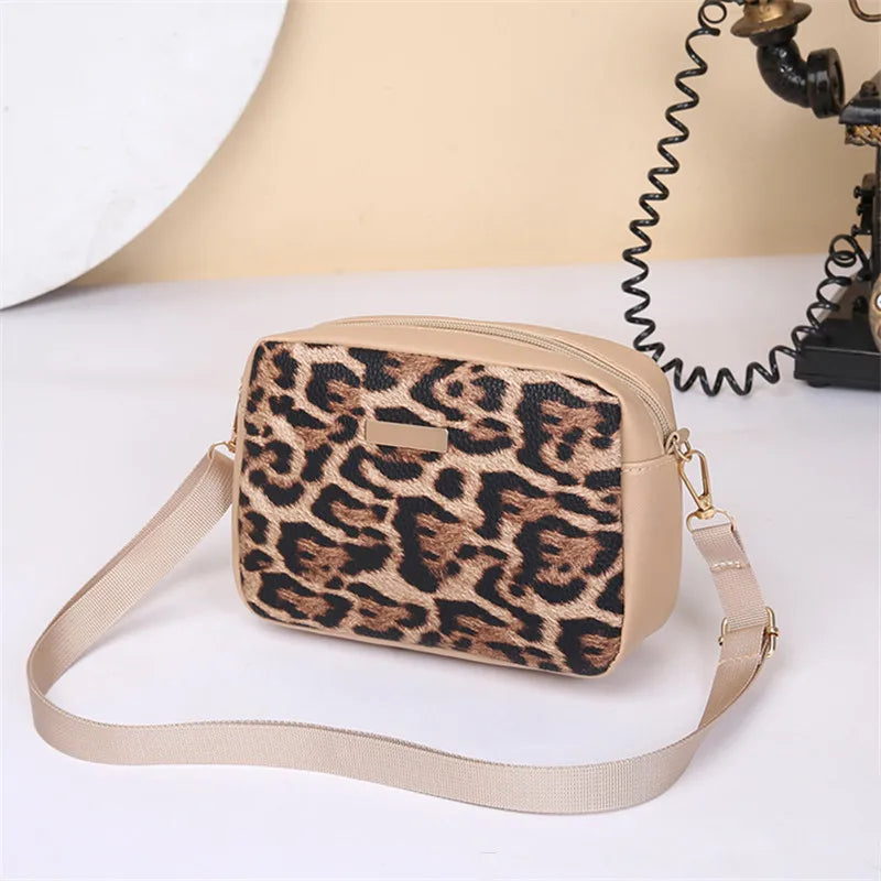 A beige leopard print crossbody bag with a tan strap resting on a white surface.