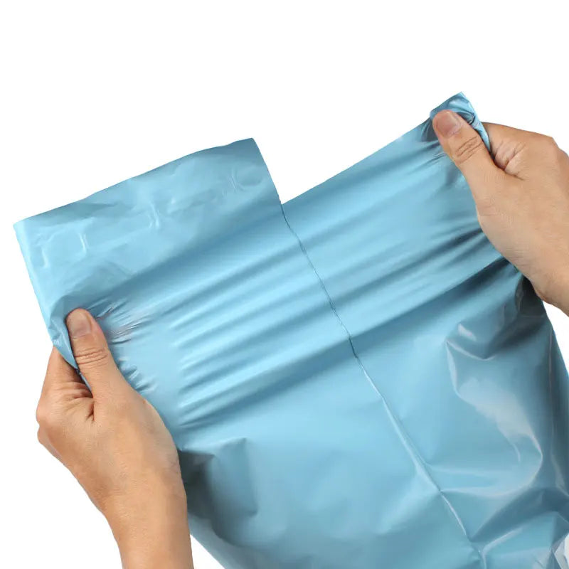 A hand is holding a light blue heavy-duty waterproof poly mailer bag, showing its flexible plastic material.