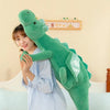 A woman is holding a large, green dragon plush toy against her chest.