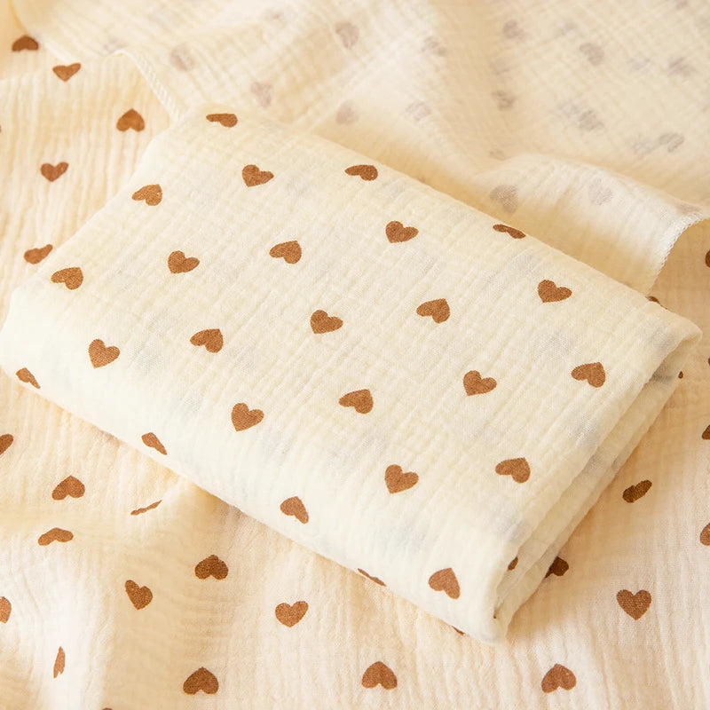 A rolled soft cotton gauze baby swaddle blanket with a subtle heart pattern on a light beige fabric.