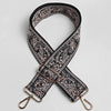 A black and beige paisley jacquard bag strap with a gold-toned buckle and leather accents.