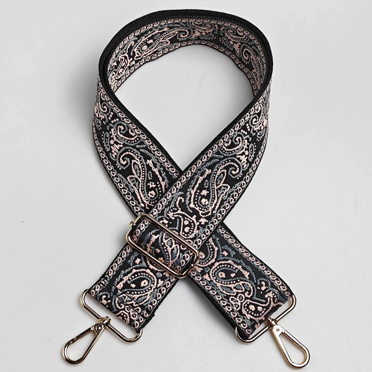 A black and beige paisley jacquard bag strap with a gold-toned buckle and leather accents.