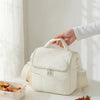 A hand is holding a cream-colored insulated lunch bag with a quilted pattern on a white table.
