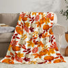 A colorful flannel throw blanket featuring an autumn pattern of orange and yellow maple leaves and pumpkins.