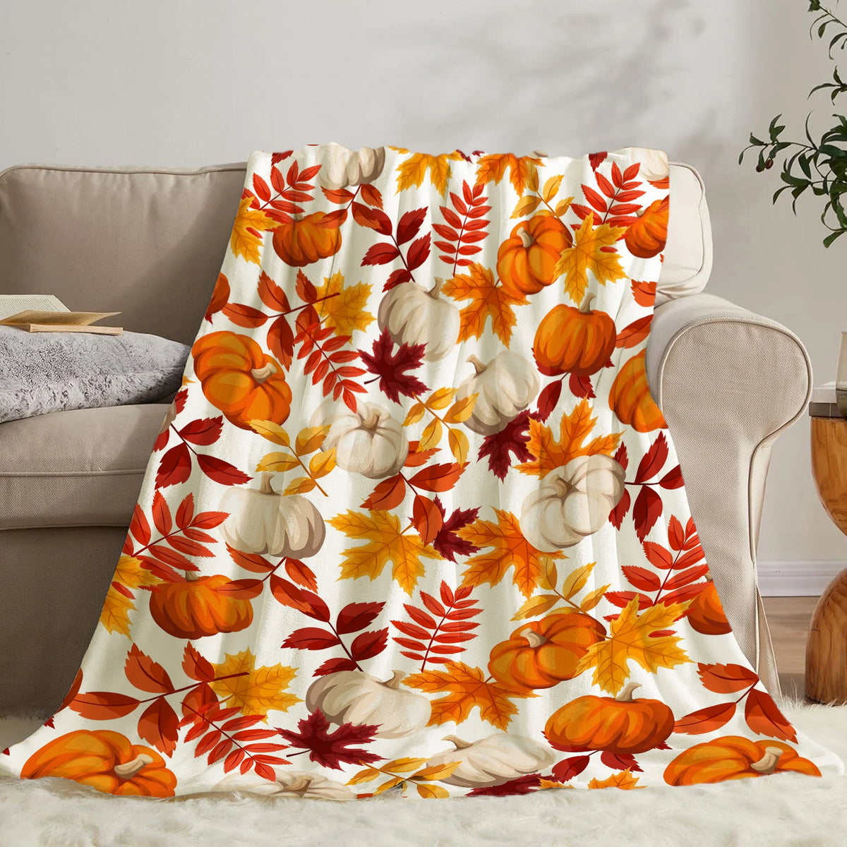 A colorful flannel throw blanket featuring an autumn pattern of orange and yellow maple leaves and pumpkins.