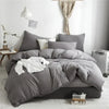 A gray duvet cover set with pom tassels and white bedding displayed on a bed.