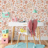 A white table with a pink chair and accessories set against a vintage floral peel-and-stick wallpaper background.