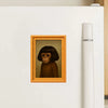 A framed picture of a monkey's face is displayed on a white refrigerator with a white bottle.