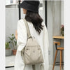 A woman wearing a beige lightweight mini backpack with an anti-theft chest strap, shown in a full-length shot.