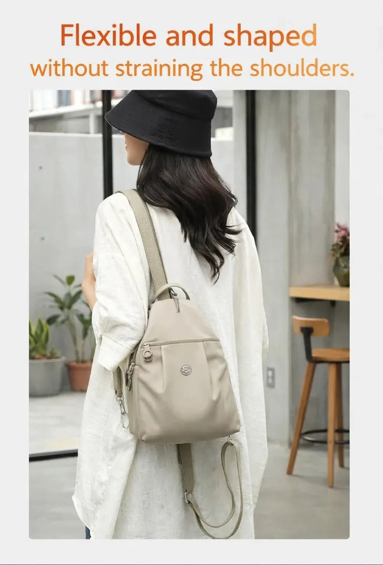 A woman wearing a beige lightweight mini backpack with an anti-theft chest strap, shown in a full-length shot.