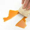 A hand is squeezing a bright orange glossy vinyl wallpaper sample onto a white surface.