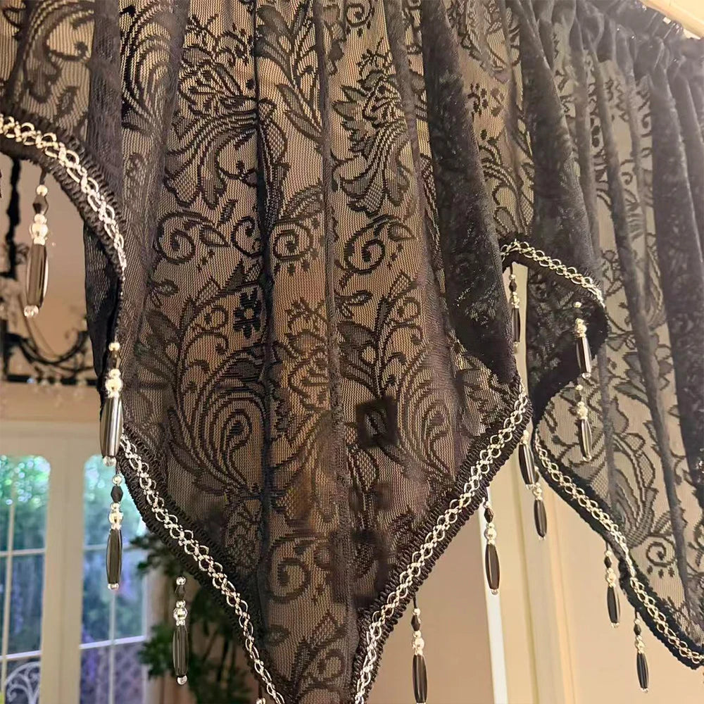 Black gothic lace curtain valance with silver trim and pendant tassels hanging in a window.