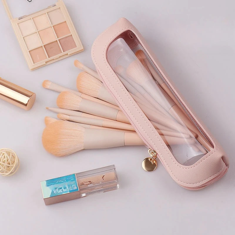 A pink leather travel makeup organizer pouch containing various makeup brushes and a small cosmetic product.