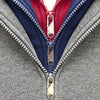 Close-up of a gray jacket featuring three colored zippers: navy, red, and gold.