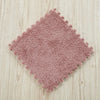A square rug made of soft, pinkish-brown plush interlocking floor tiles on a light wooden surface.