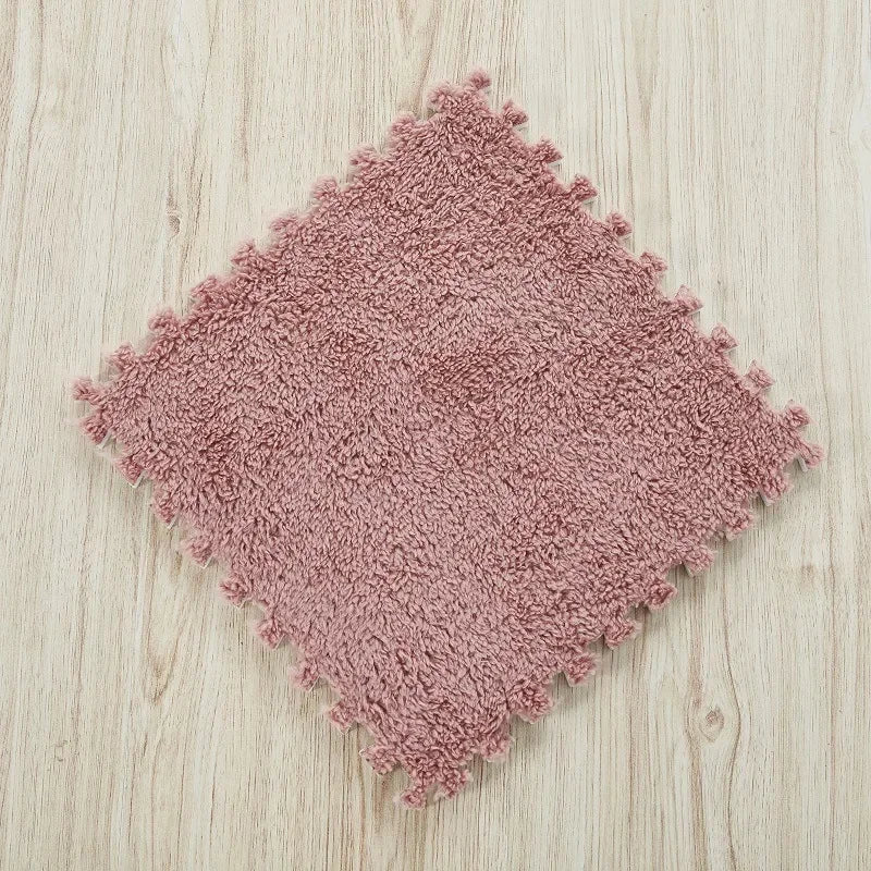 A square rug made of soft, pinkish-brown plush interlocking floor tiles on a light wooden surface.