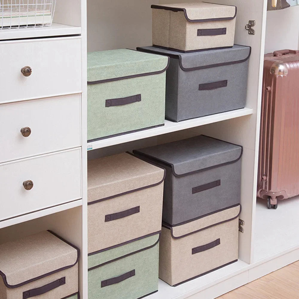 A set of fabric storage boxes in gray, green, and beige stacked on a white shelf.