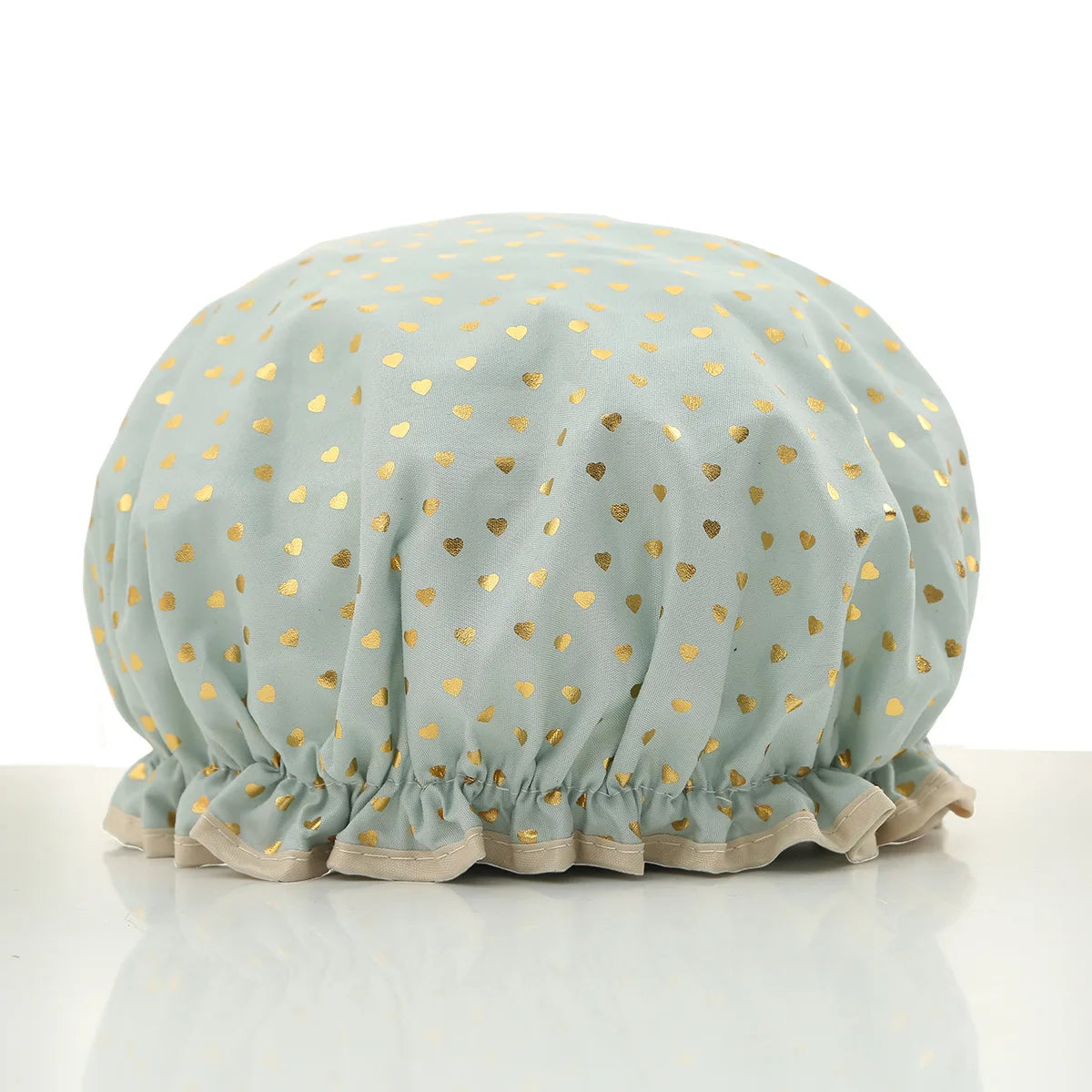 A light mint green reusable elastic shower cap decorated with gold heart patterns.