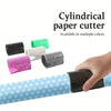 A hand is using a cylindrical paper cutter with a sliding blade, shown alongside various colored cutters.