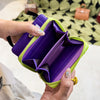 A hand holds a purple and lime green compact wallet with a black keychain against a patterned fabric background.