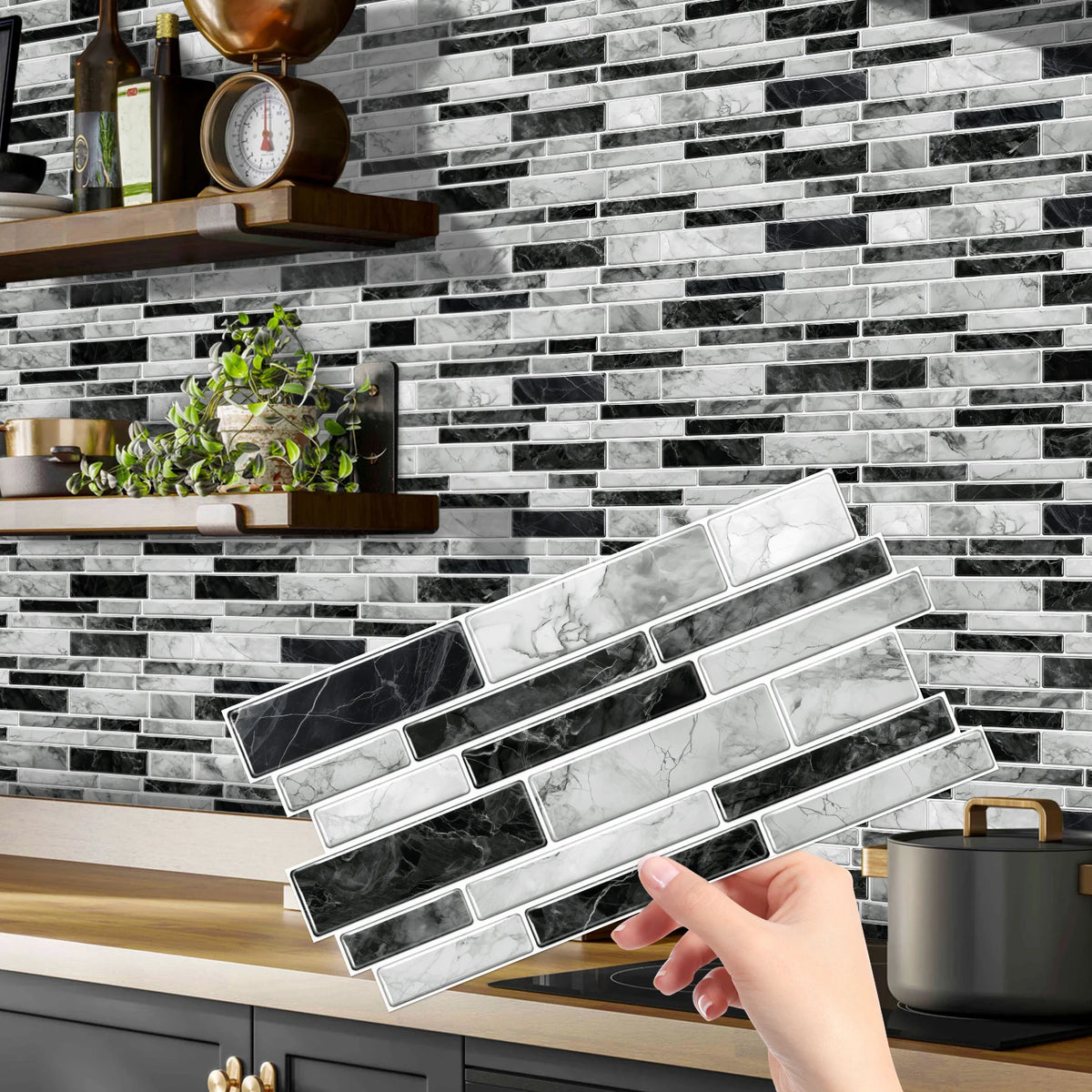 A hand holds a rectangular tile sticker for kitchen backsplash against a dark gray and white marble subway tile wall.
