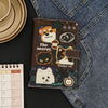 A brown leather passport holder featuring various cartoon cats and an apple design against a dark background.