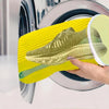 A hand holds a yellow reusable mesh shoe washing bag with a green athletic shoe inside, positioned above a washing machine dr