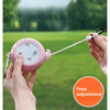 A hand is holding a pink retractable clothesline with a white cord, set against a blurred green outdoor background.