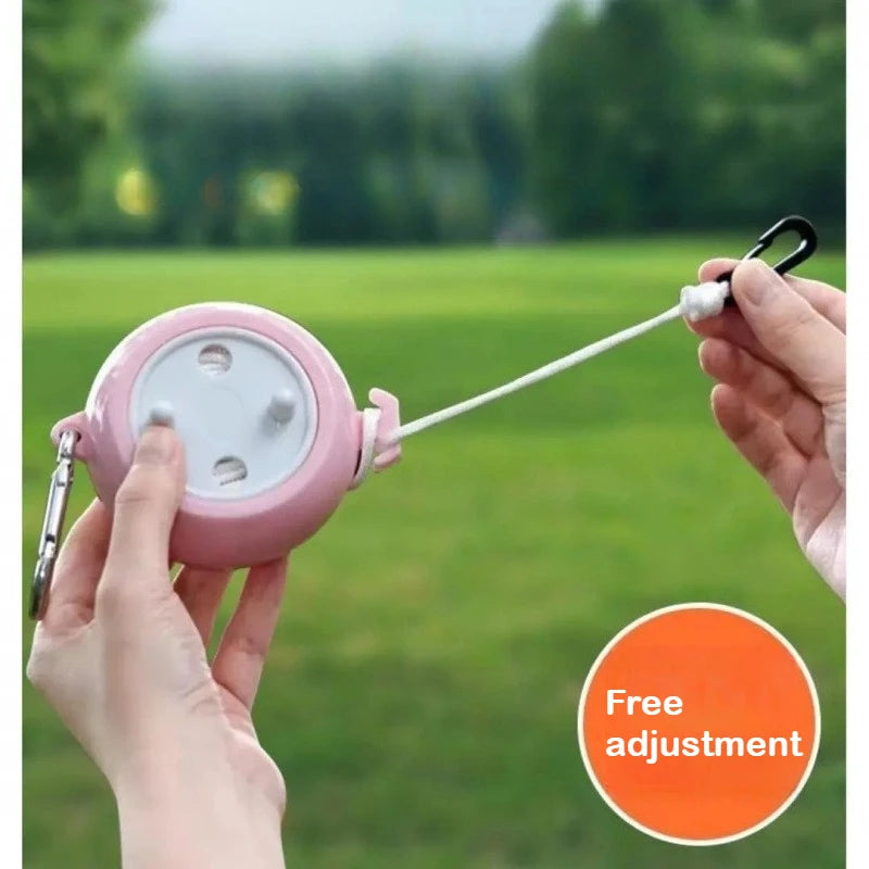 A hand is holding a pink retractable clothesline with a white cord, set against a blurred green outdoor background.