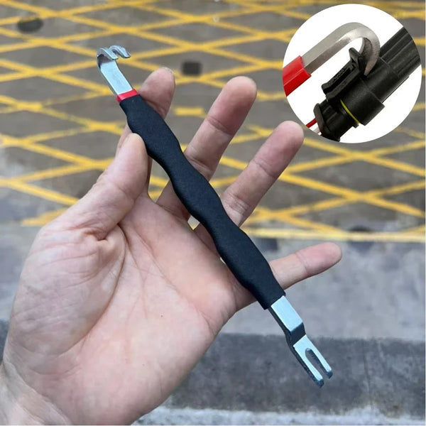 A hand holds an automotive electrical connector removal tool, showing the tool and a disassembled connector tip.