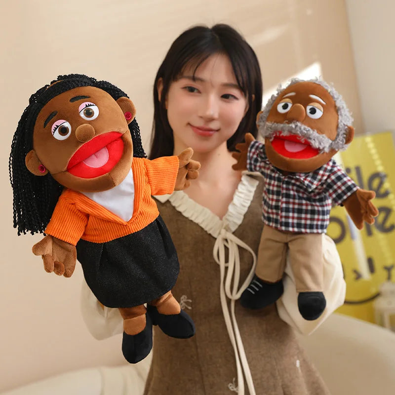 A woman holds two hand puppets, one black and orange, and another brown with a white beard, against a light background.